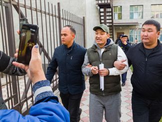 Non-uniformed officers escort blogger and activist Atai Beishenbek, a defendant in the “Kempir-Abad case,” out of a Bishkek courthouse after his sentencing. October 25, 2022.