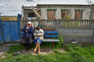 Люди отдыхают на скамейке у поврежденных домов в селе Загальцы под Киевом