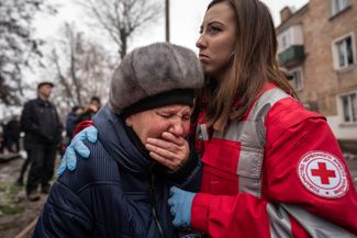 Сотрудница Красного Креста успокаивает местную жительницу возле разрушенного дома в Кривом Роге