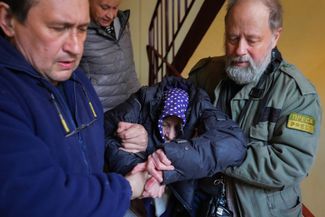 Волонтеры помогают пожилой женщине спуститься в бомбоубежище в Харькове. 25 марта 2022 года