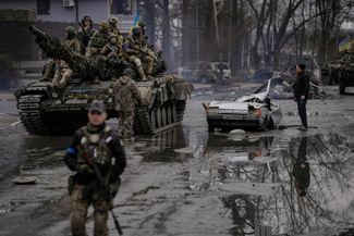Украинские военные едут на танке мимо разрушенного автомобиля. В нем до сих пор находится тело водителя. Киевская область