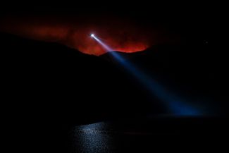 Пожарный вертолет над озером Пиру в Калифорнии на фоне зарева от обширных лесных пожаров, охвативших штат. 17 августа 2020 года