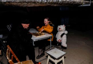 Семилетняя девочка играет в шахматы со своим дедушкой в ​​подвале жилого дома в пригороде Харькова