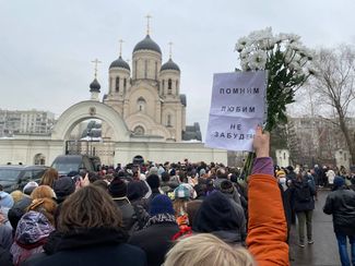 A mourner outside the cemetery where Navalny was buried holds up a sign that says, “We remember, we love, we won’t forget.”