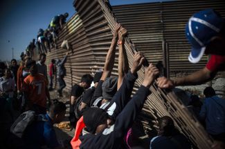 Мигранты пытаются перебраться через ограждения, установленные на мексиканской стороне границы с США