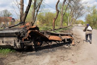 Житель села Термаховка, которое около месяца было оккупировано российскими военными, проходит мимо сгоревшей военной техники.