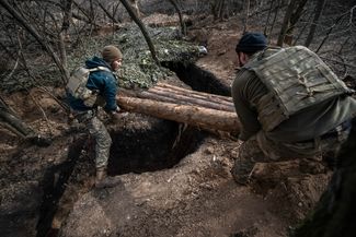 Украинские солдаты размещают бревна над траншеей