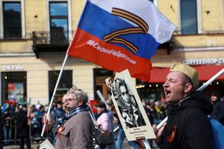 Участник «Бессмертного полка» в Петербурге несет флаг с георгиевской лентой в виде буквы Z