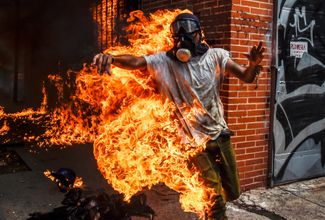 Демонстрант загорелся при взрыве полицейского мотоцикла во время беспорядков в Венесуэле. Уличные протесты были вызваны планами президента Николаса Мадуро переписать конституцию. Каракас, 3 мая