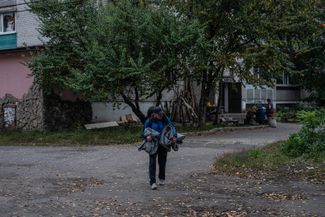 Мужчина несет одеяла мимо поврежденныхмногоквартирных домов в Святогорске, где по-прежнему нет воды и электричества