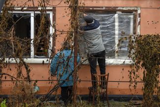 Местные жители заклеивают пленкой окно своего дома, разбитое во время боев