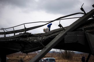 Волонтер тащит тележку с едой по разрушенному мосту в городе Ирпень под Киевом