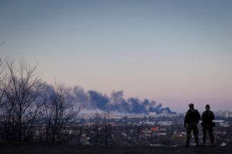 Украинские солдаты смотрят на столб дыма, который поднимается от хлебозавода «Кулиничи» после обстрела Харькова