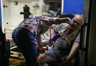 Медработница оказывает помощь мужчине, пострадавшему в результате обстрела в Донецке