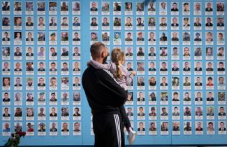 Мужчина и его дочка в Киеве смотрят на фотографии погибших украинских военных на мемориале, посвященном памяти погибших защитников страны