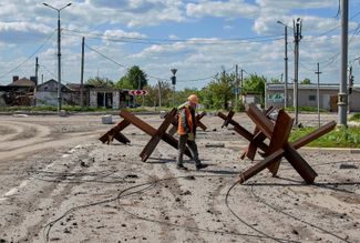 Рабочий коммунальных служб идет мимо противотанковых ежей в Северной Салтовке — одном из районов Харькова. 23 мая 2022 года