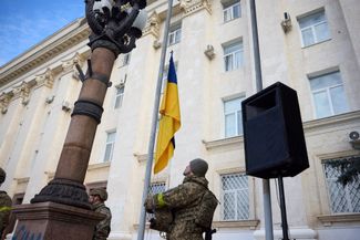 Военнослужащий ВСУ поднимает флаг Украины на одной из центральных улиц Херсона