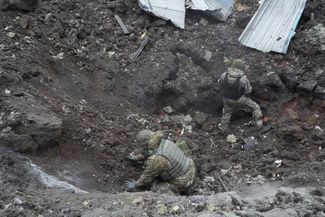 Украинские полицейские осматривают воронку возле жилого дома, поврежденного российским ракетным ударом