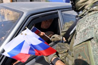 Сотрудник военной полиции Геническа раздает флажки автомобилистам на блокпосту