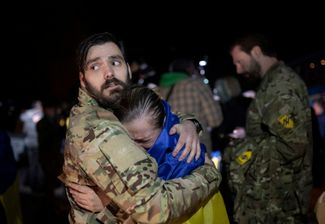 Освобожденная из российского плена женщина обнимает мужчину в камуфляжной форме после прибытия в Запорожье