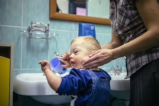 A caregiver helps a child wash his face