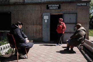 60-летняя жительница Северодонецка, административного центра Луганской области, стоит у входа в офис ритуальных услуг, ставший приютом во время войны — там она теперь живет и работает.