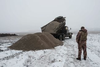 Украинский военный наблюдает за разгрузкой стройматериалов на фортификационной линии под Бахмутом