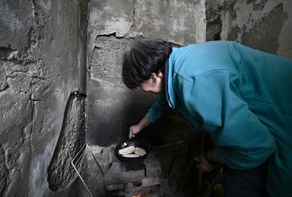 62-летняя Нина жарит пирожки на импровизированной дровяной печи у входа в подвал. 