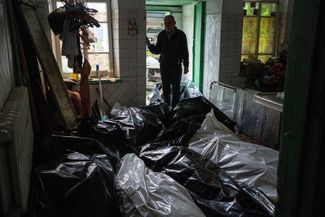 Доктор смотрит на тела в пластиковых мешках в морге изюмского госпиталя