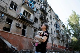 Жительница Краматорска с собакой на руках смотрит на дом, пострадавший из-за ракетного удара войск РФ по жилым кварталам