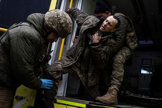Украинские военные врачи помогают раненому бойцу ВСУ выбраться из машины скорой помощи, прибывшей с поля боя, чтобы отнести его в полевой госпиталь