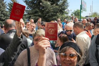 People in Luhansk hold up their passports ahead of the opening of a center where they can submit documents to obtain Russian citizenship