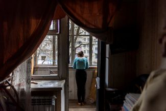 Алена из Харькова выглядывает на улицу из окна своей квартиры, поврежденной в результате артиллерийского обстрела