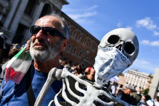 Ковид-отрицатель со скелетом в маске, на которой написано «Я умер не от коронавируса, а от голода». Рим, 10 октября 2020 года