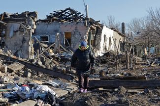 Местная жительница на фоне домов, разрушенных, по утверждению назначенных Россией властей города, в результате украинского обстрела. 