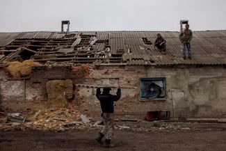 Рабочие в деревне Малая Рогань Харьковской области чинят крышу коровника, поврежденную минометным снарядом.