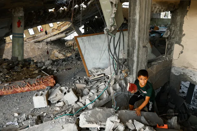 Мальчик с книгой среди завалов в одном из разрушенных домов города Хан-Юнис