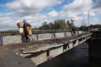 Украинские военные идут по поврежденному мосту, ведущему в недавно освобожденный город Купянск