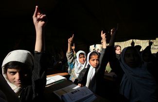 Девочки-афганки тянут руки во время урока английского в Кабуле. В переполненной школе, сделанной из палаток для беженцев в разрушенных войной зданиях, учатся более шести тысяч человек, почти все — девочки. Школа работает в три смены. 22 ноября 2006 года