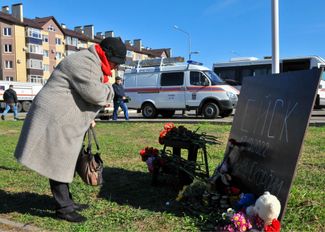 Женщина молится, возлагая цветы к доске с надписью «Ейск 17.10.2022 Помним. Скорбим» у места крушения