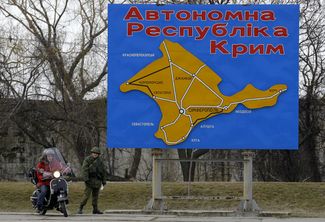 Российский военнослужащий в форме без опознавательных знаков у плаката с картой Крыма в Керчи, 3 марта 2014 года
