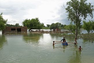 Жители деревни в округе Раджанпур (провинция Пенджаб) используют плот для перемещения по затопленной местности. Спасатели до сих пор не могут добраться до многих районов, где люди ждут эвакуации<br>