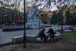 Жители Николаева играют в шахматы возле памятника, обложенного мешками с песком для защиты от обстрелов
