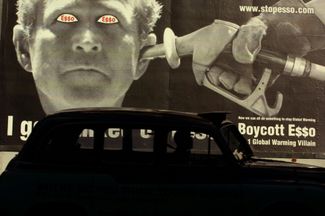Такси у рекламного щита неподалеку от лондонской штаб-квартиры компании Exxon Mobil летом 2001 года. Снимок сделан во время протестной кампании против предполагаемых нарушений прав человека в странах добычи нефти, где работает Exxon Mobil, а также против лоббистких усилий ее менеджеров по отмене Киотского соглашения об изменении климата.