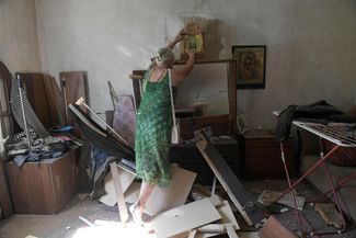 Любовь Толчина снимает икону со стены в разрушенном доме своего сына, погибшего после обстрела ВСУ