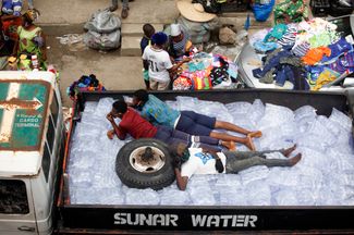 Мужчины лежат на пакетах с водой, предназначенных для продажи на рынке нигерийского города Лагос, 20 мая 2020 года