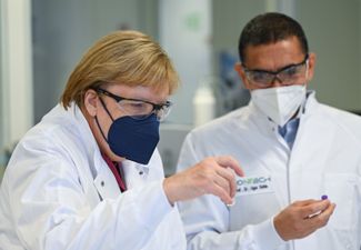 Угур Шахин, основатель и глава компании BioNTech, показывает канцлеру Германии Ангеле Меркель образец ампул для вакцины от ковида BioNTech/Pfizer во время официального визита канцлера на комплекс компании по производству вакцин в Германии. Марбург, 19 августа 2021 года