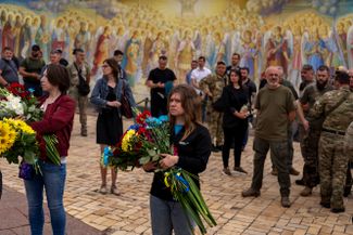 Женщины с цветами встречают траурную процессию, выносящую тело украинского снайпера-разведчика Тенгри в Киеве. Личность убитого не была раскрыта даже после смерти, на портретах его лицо закрыто маской