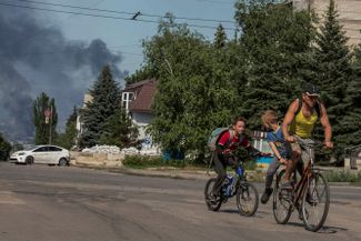 Житель Лисичанска с детьми уезжает на велосипеде от места взрыва
