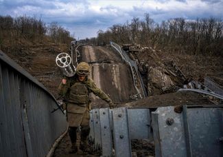 A Ukrainian soldier carries an empty cluster cartridge from a MLRS BM-27 Uragan missile while walking along a bridge that was destroyed near the city of Bakhmut. March 8, 2023.